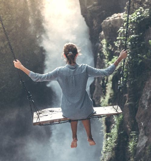 Image of a woman sitting on an oversized swing over a chasm, with back to camera