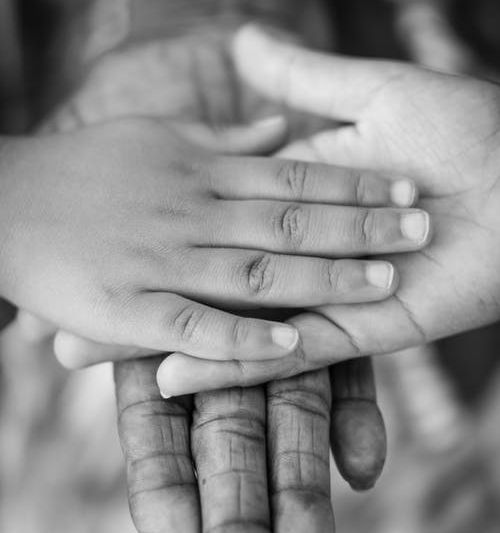 Black and white image of three individuals' outstretched hands, placed on top of each other