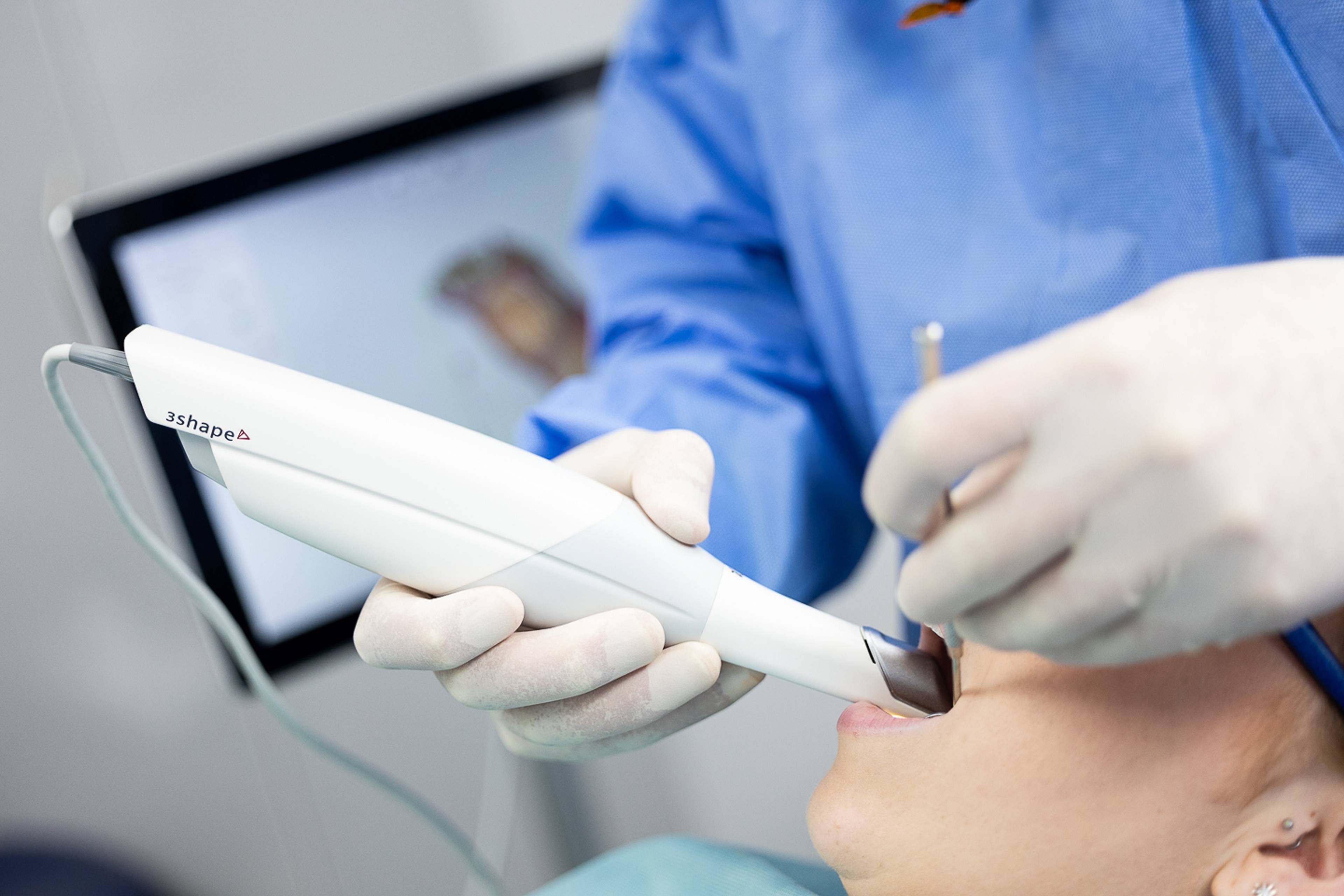 Dentist wearing white gloves scanning patient's teeth with a 3D intra-oral scanner 