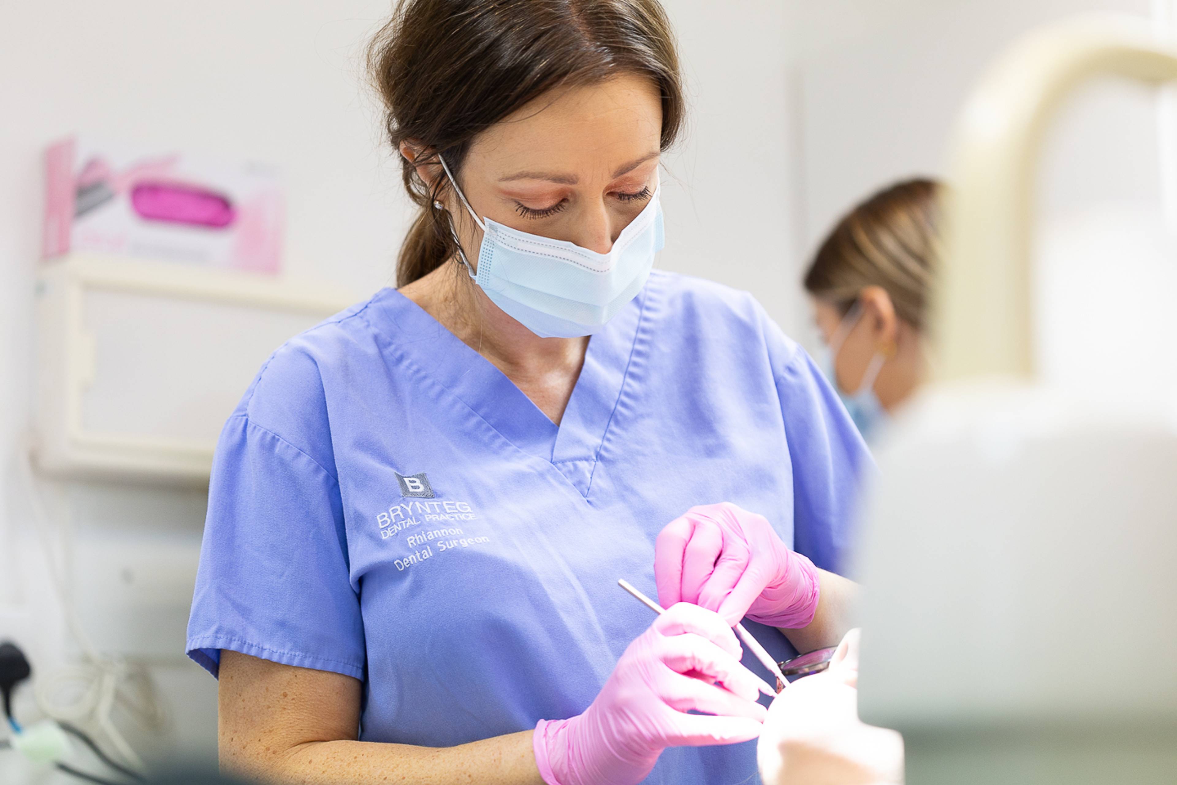 Dentist in blue scrubs and pink gloves providing routine dental care with instruments