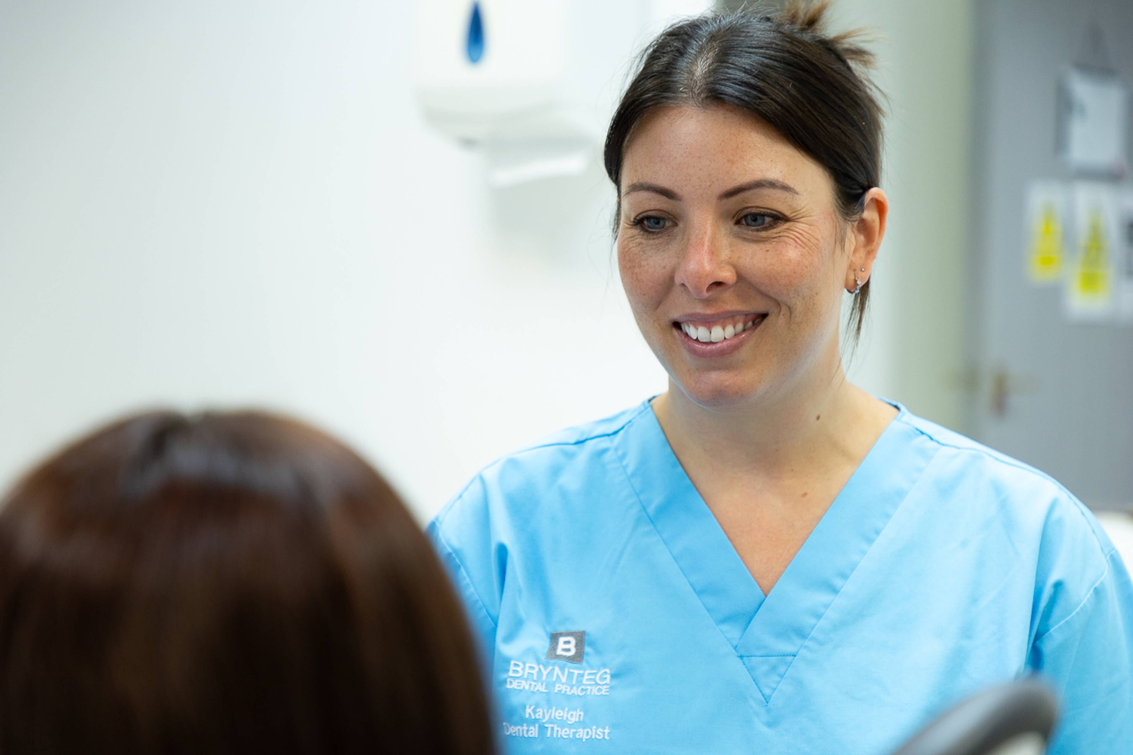 Female dentist in blue scrubs smiling at patient