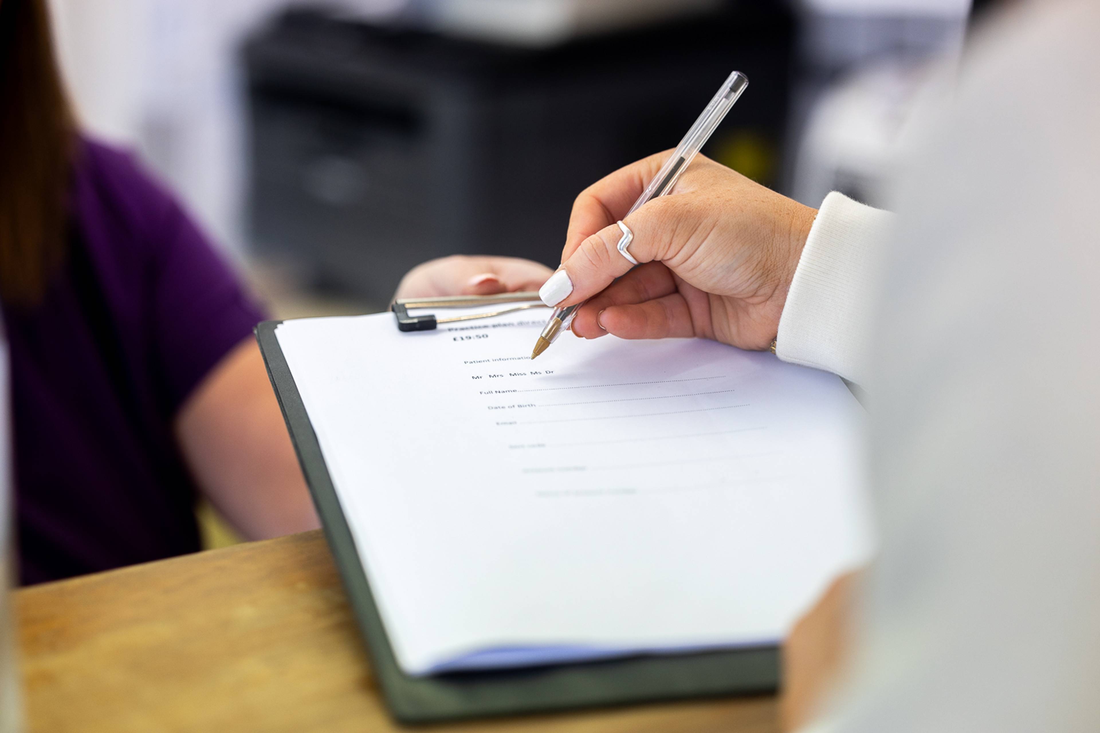 Dros ysgwydd claf yn llofnodi ffurflen gyda beiro yn y dderbynfa