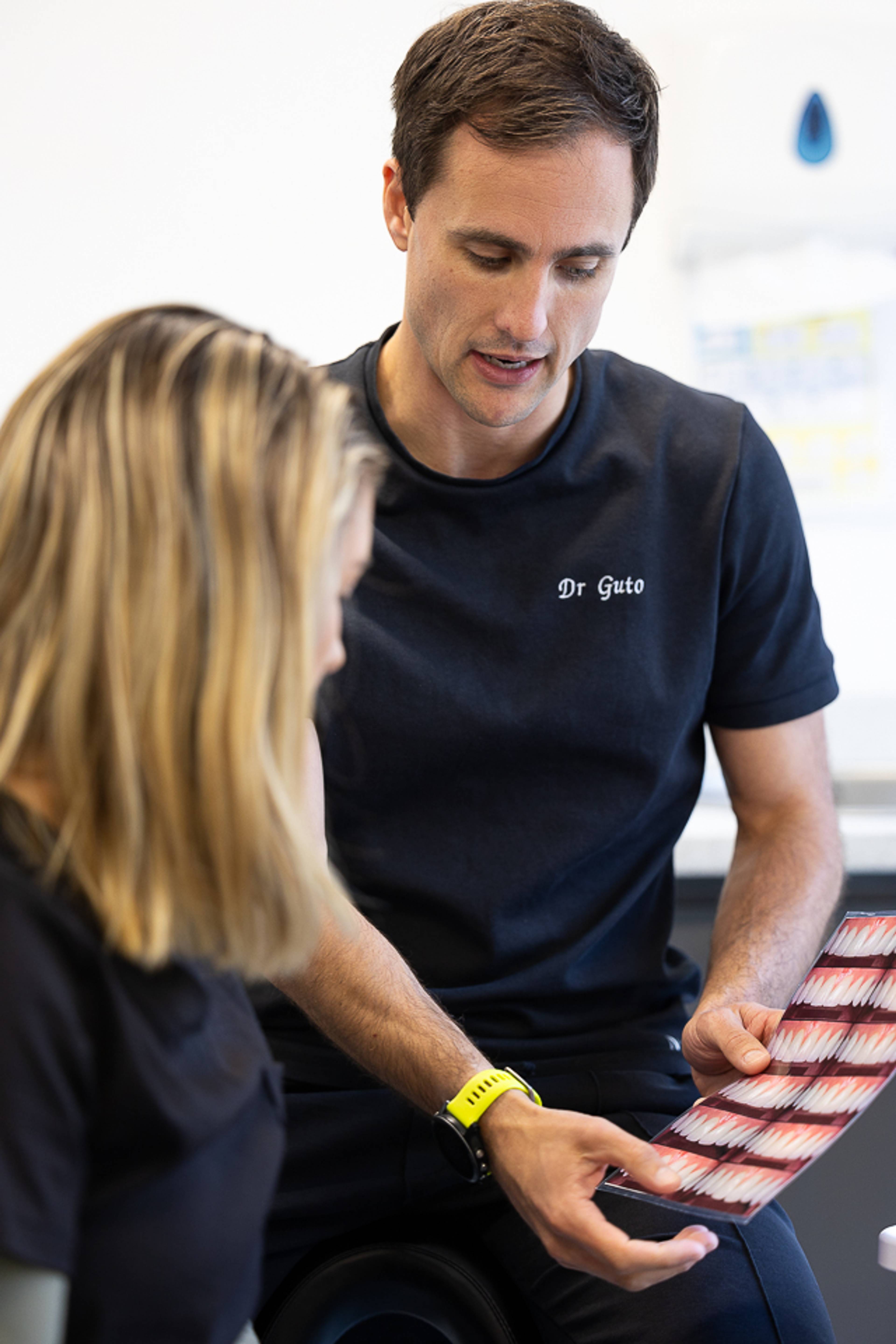 Deintydd yn esbonio'r driniaeth i'r claf gan gyfeirio at luniau