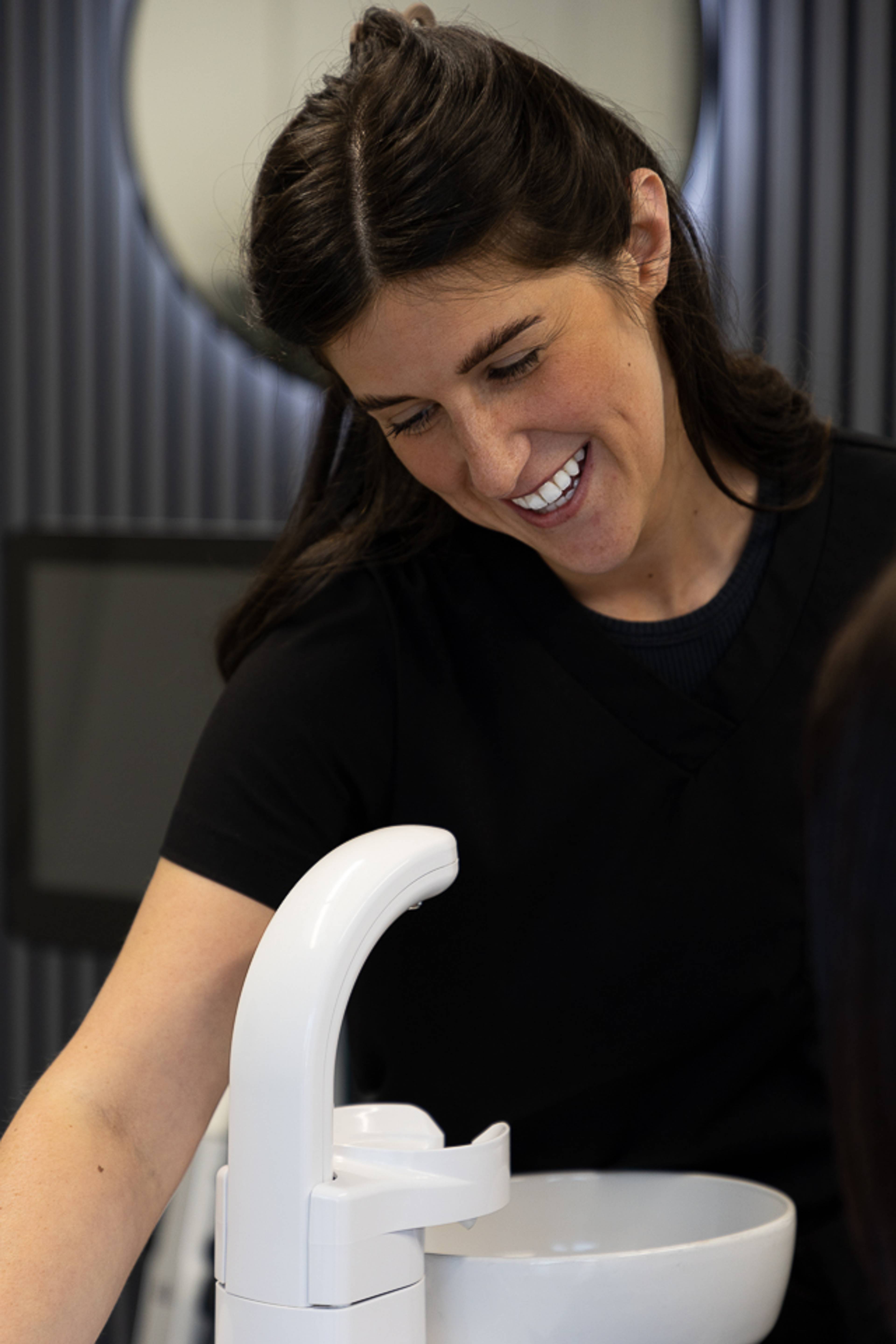 Nyrs yn gwenu wrth helpu i berfformio triniaeth mewn deintyddfa