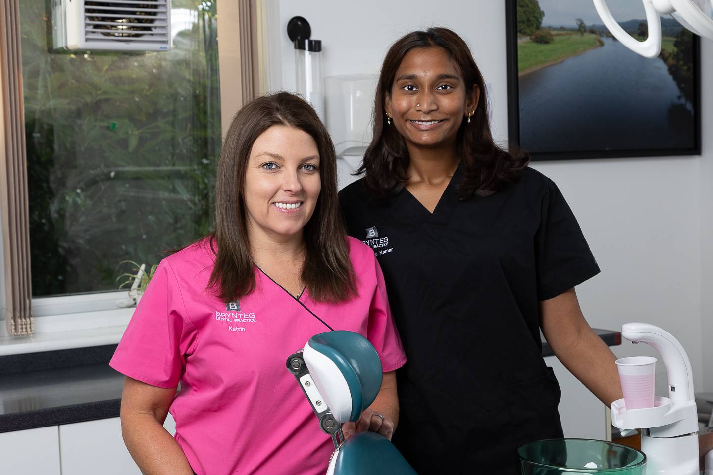 Nyrs a deintydd yn gwenu tuag at gamera