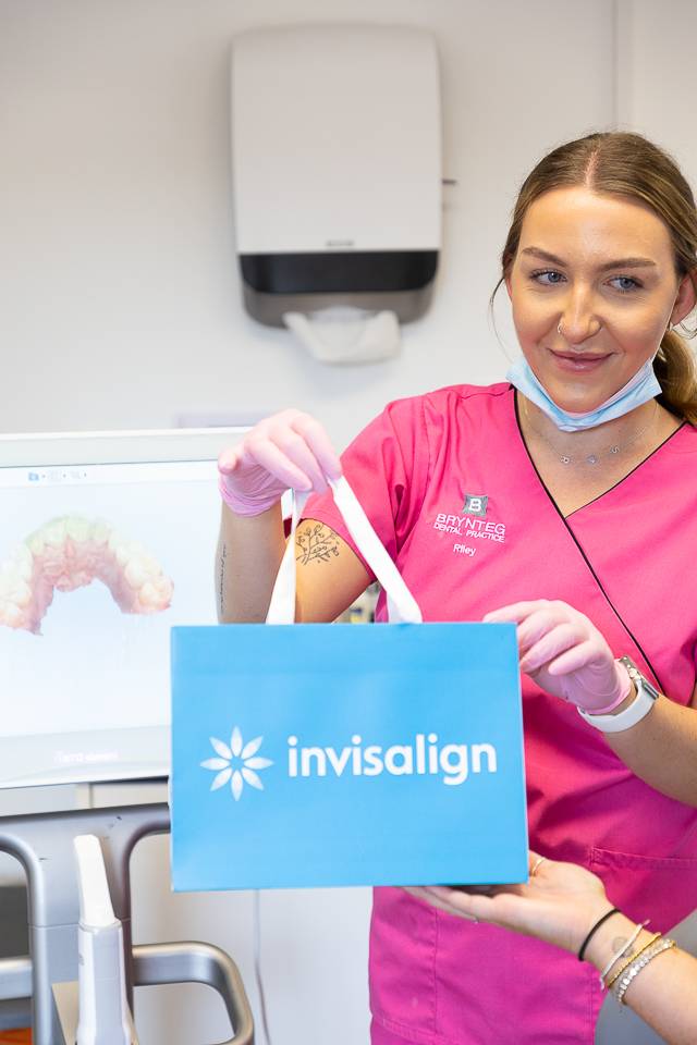 Nurse in pink scrubs holding a blue Invisalign bag handing it to the patient