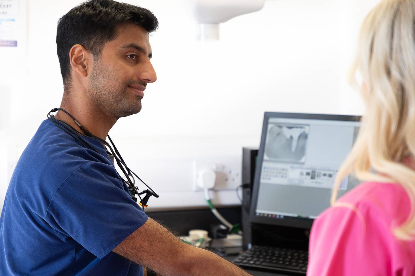Dentist sat at computer explaining to patient veneer treatment