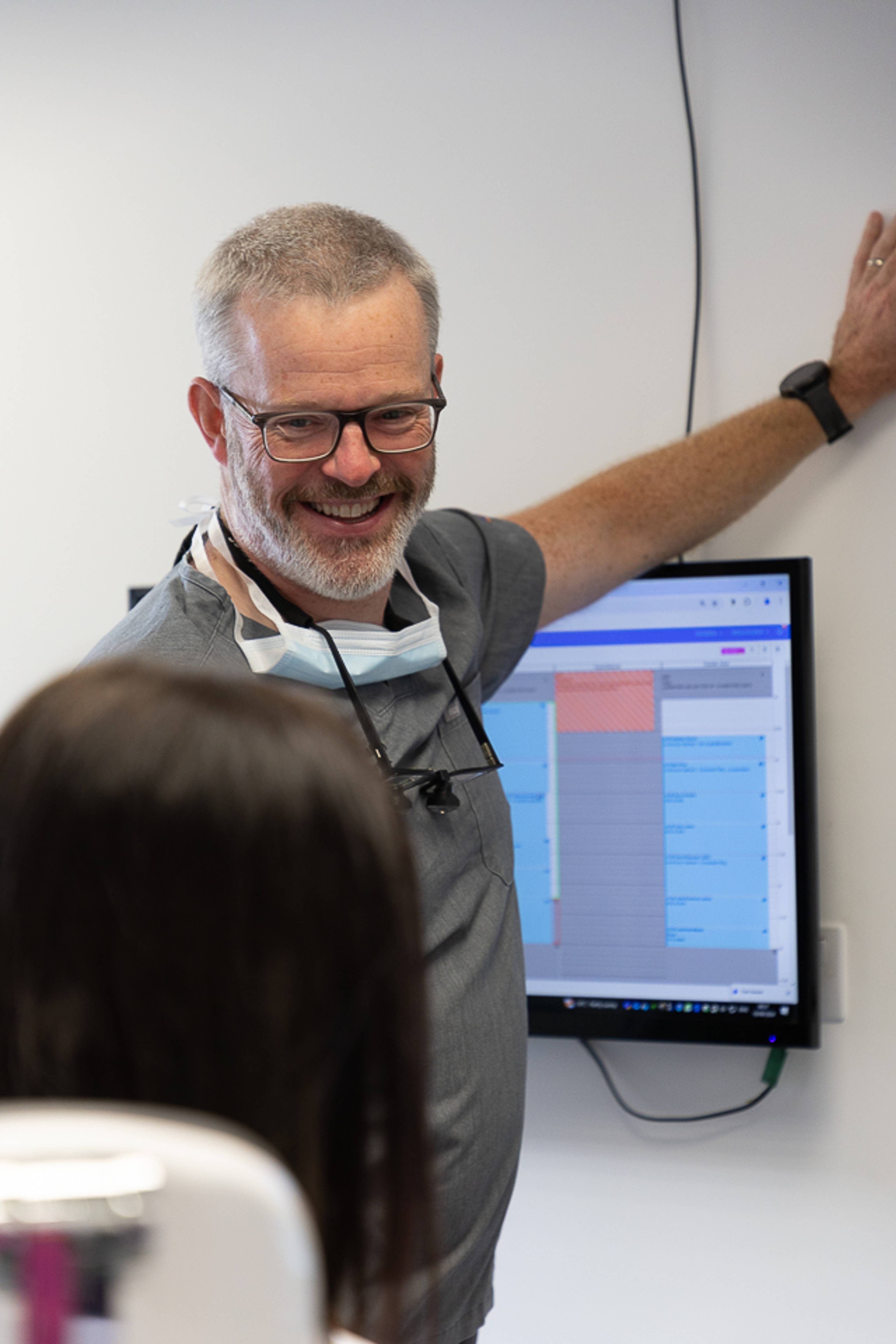 Deintydd yn gwenu ac yn disgrifio triniaeth i'r claf