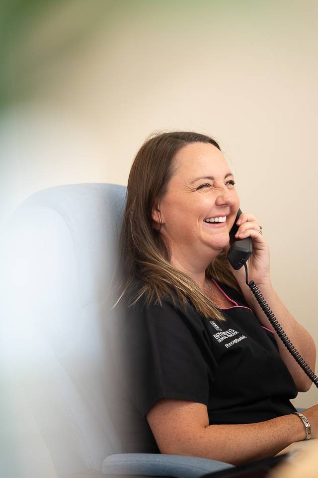 Derbynnydd mewn sgrwbiau du yn chwerthin ar y ffôn i'r claf