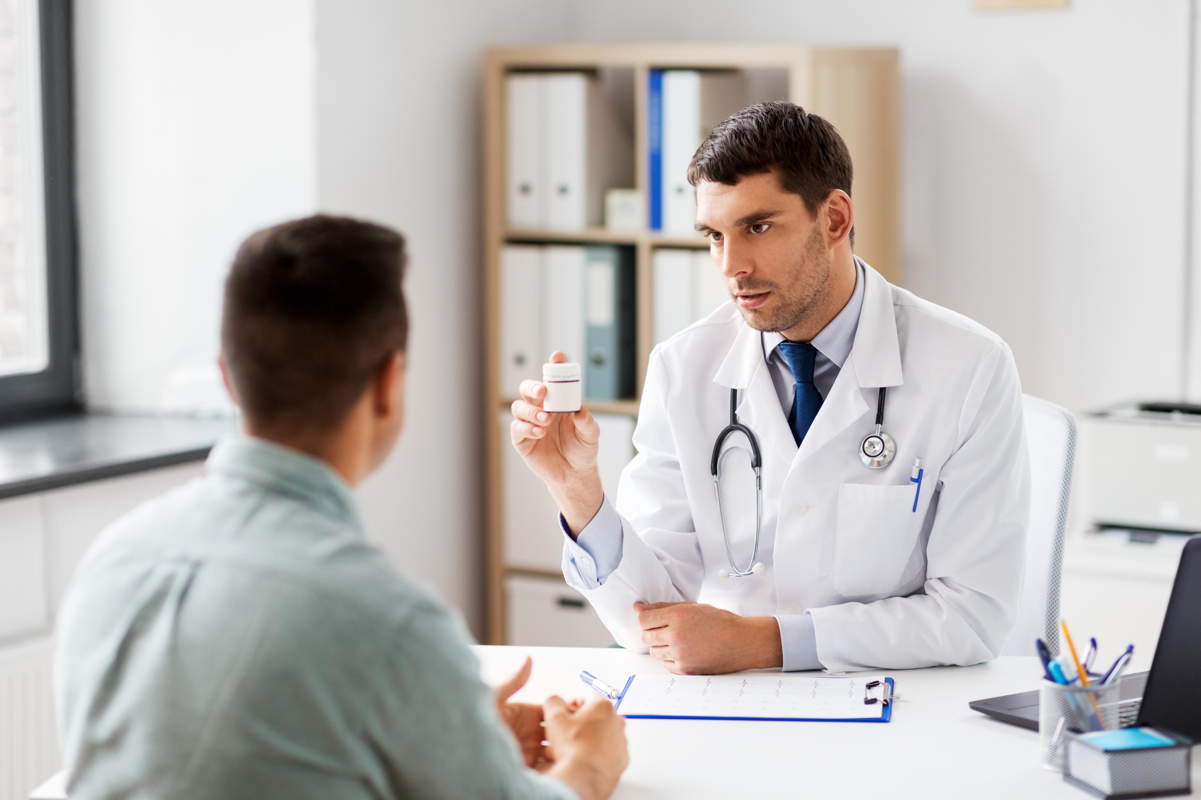 Young male doctor consulting with male patient facing away from camera; clinical setting