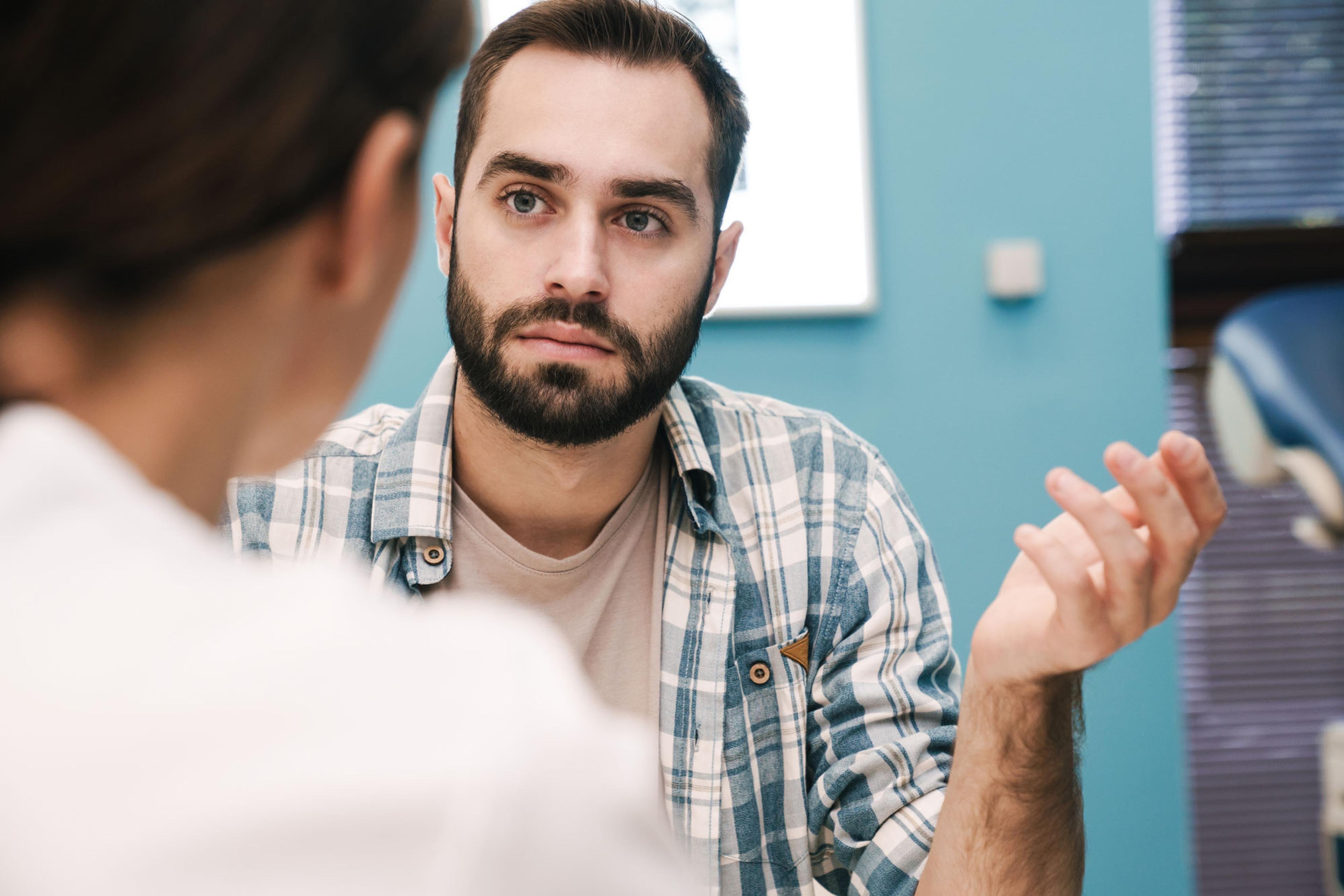 A young man discussing differences between finasteride vs minoxidil with his doctor.