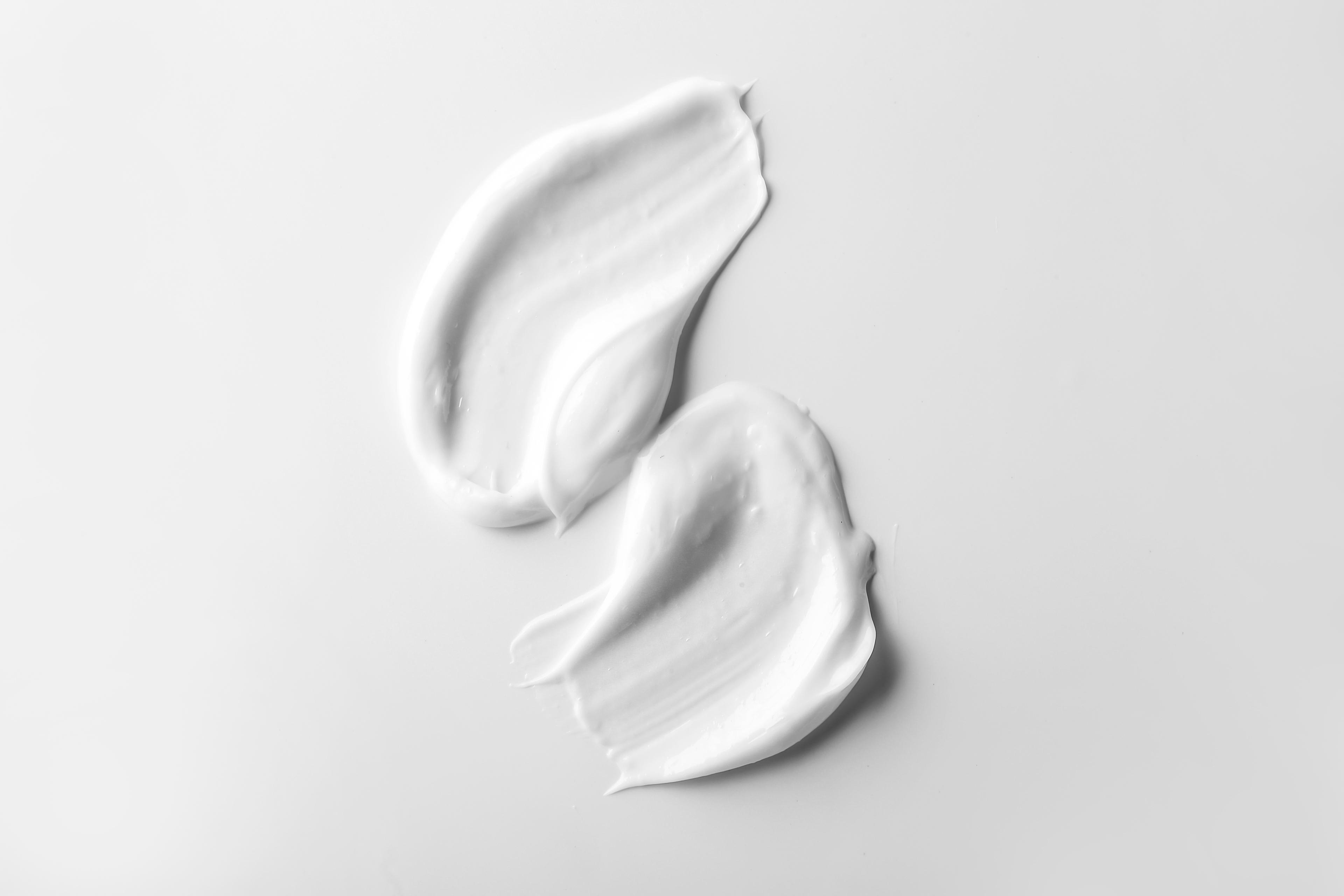 Two smears of topical finasteride gel or cream on a white background.