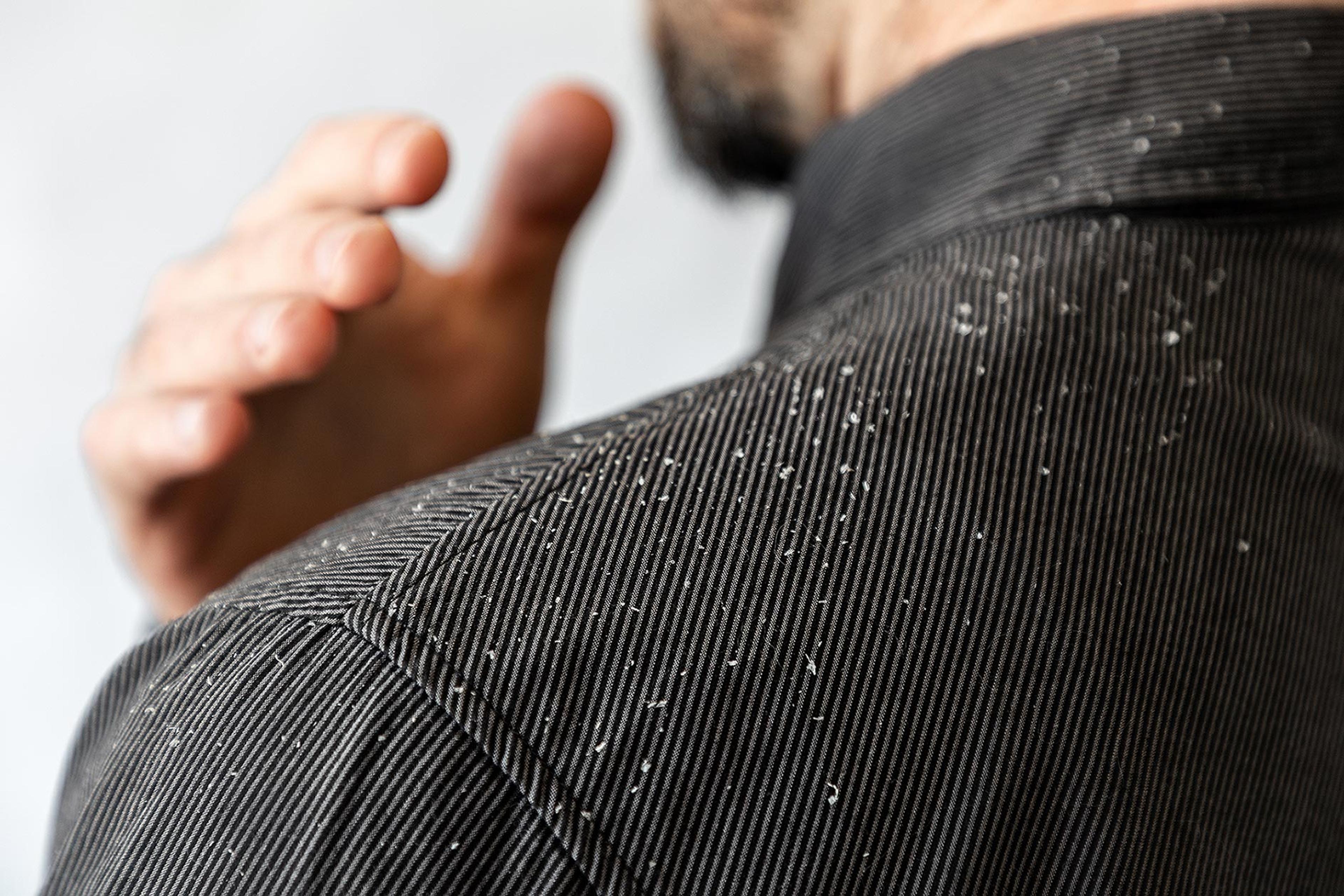 Man wearing black dress shirt  brushing visible white flakes of his left shoulder.