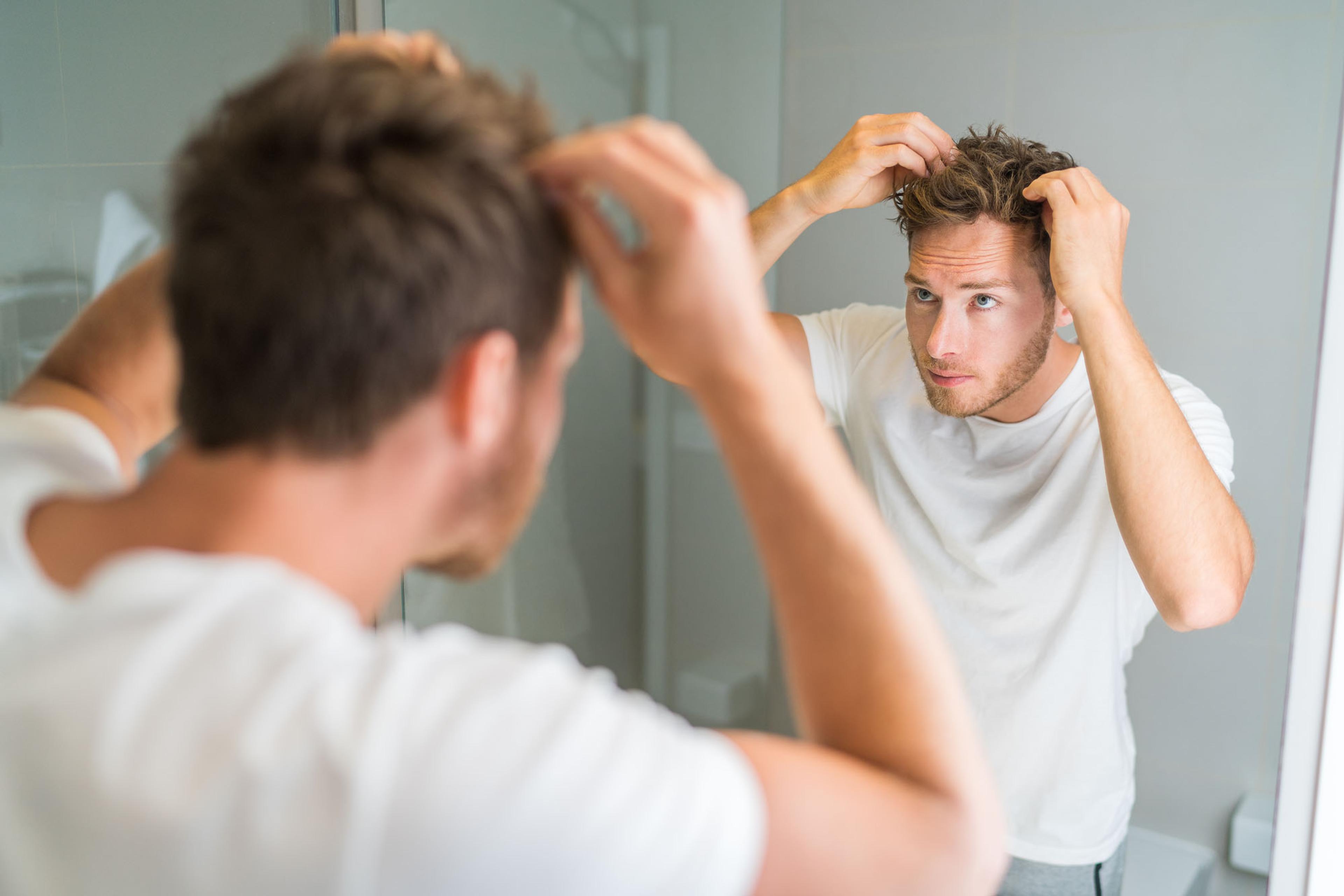 Young man looking at hair in mirror considering finasteride for hair loss.