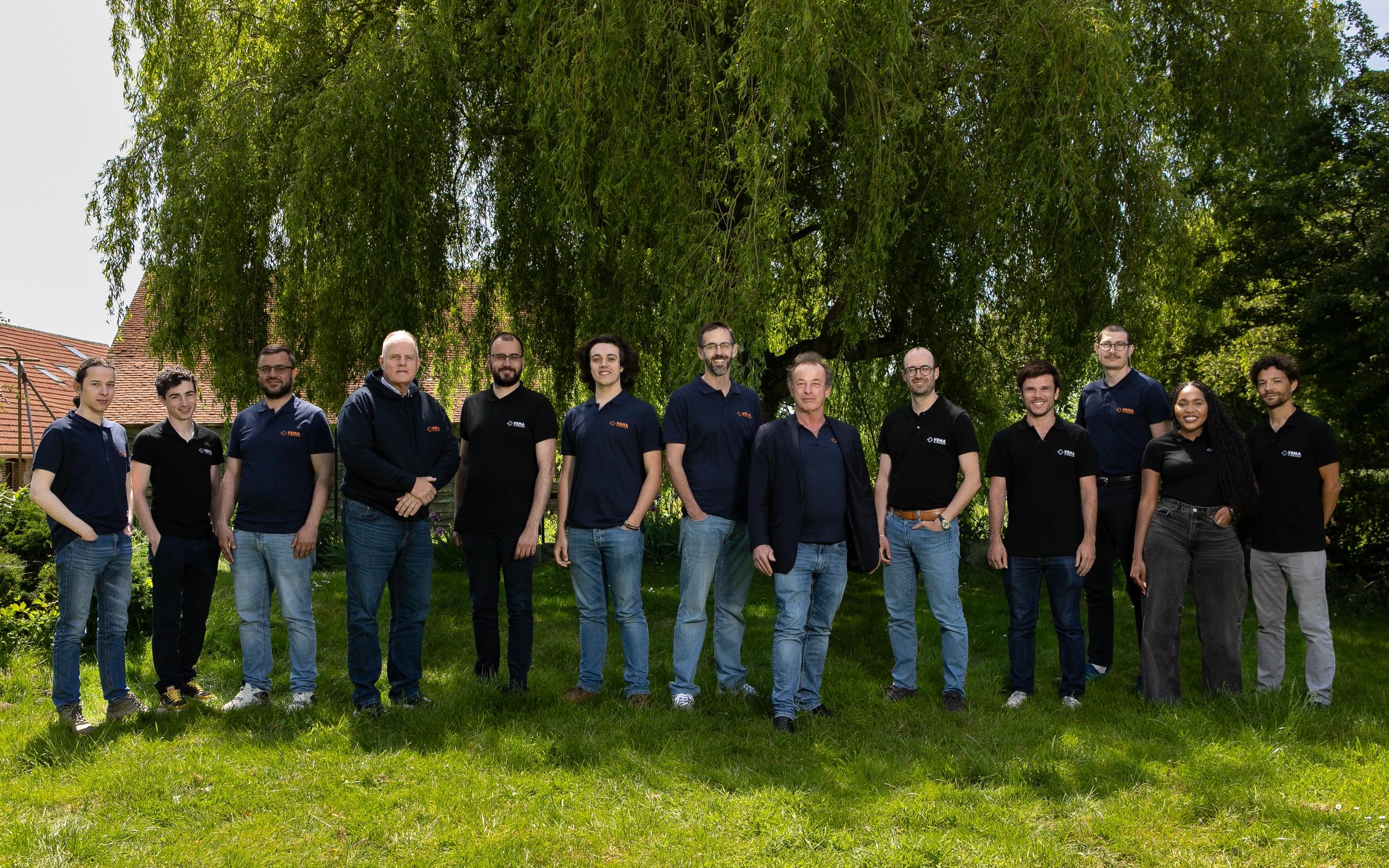 Team members of Vema Hydrogen standing together outdoors on a sunny day, posing for a group photo in front of a large leafy tree.