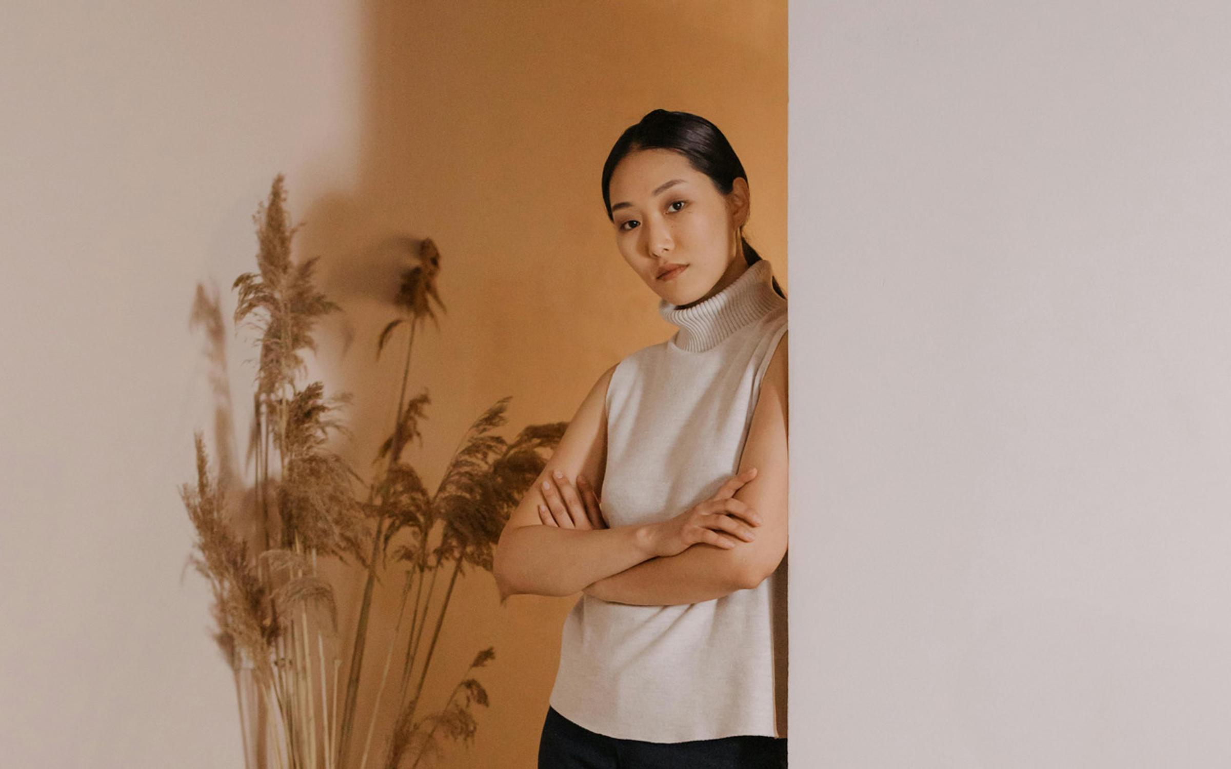 Portrait of a calm woman in a sleeveless turtleneck standing by a neutral-toned wall, reflecting the quiet strength and natural aesthetics behind Merino Energy’s innovation.
