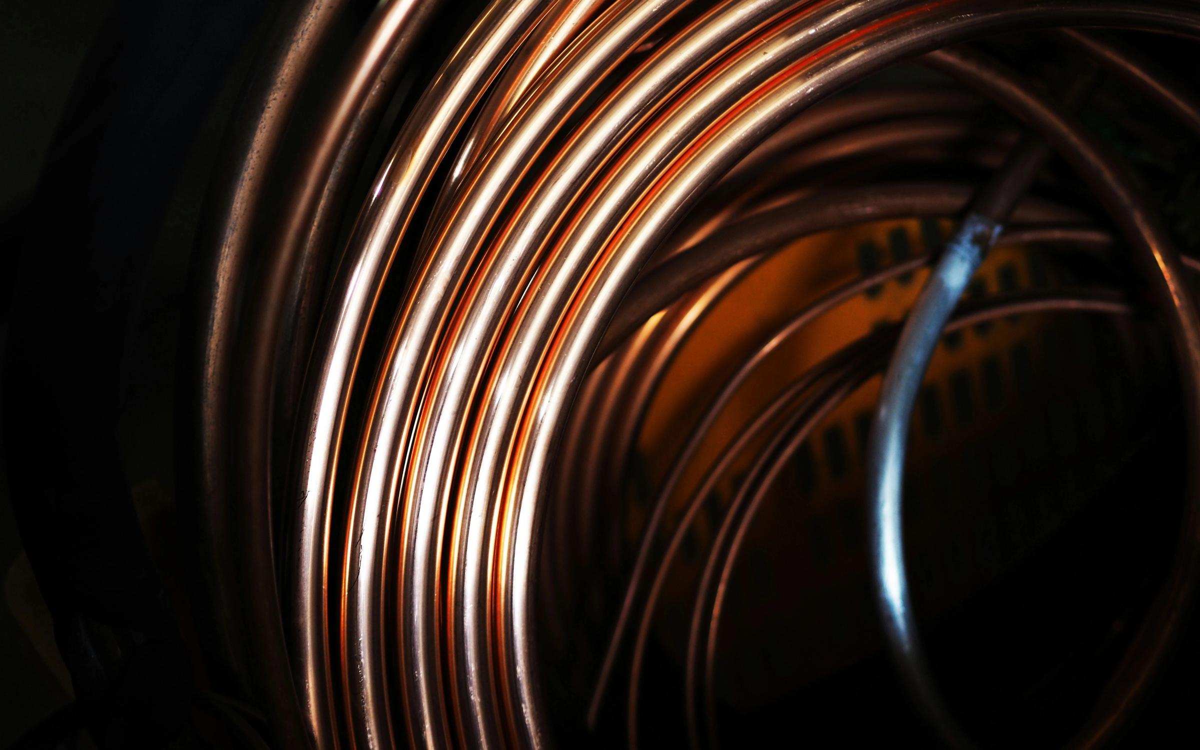 Close-up view of coiled copper wire with rich metallic tones and dramatic lighting, highlighting the texture and curvature of the metal.