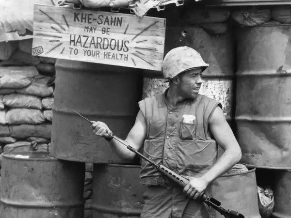 U.S. Marine standing in front of a sign reading 'Khe Sanh can be hazardous for your health'