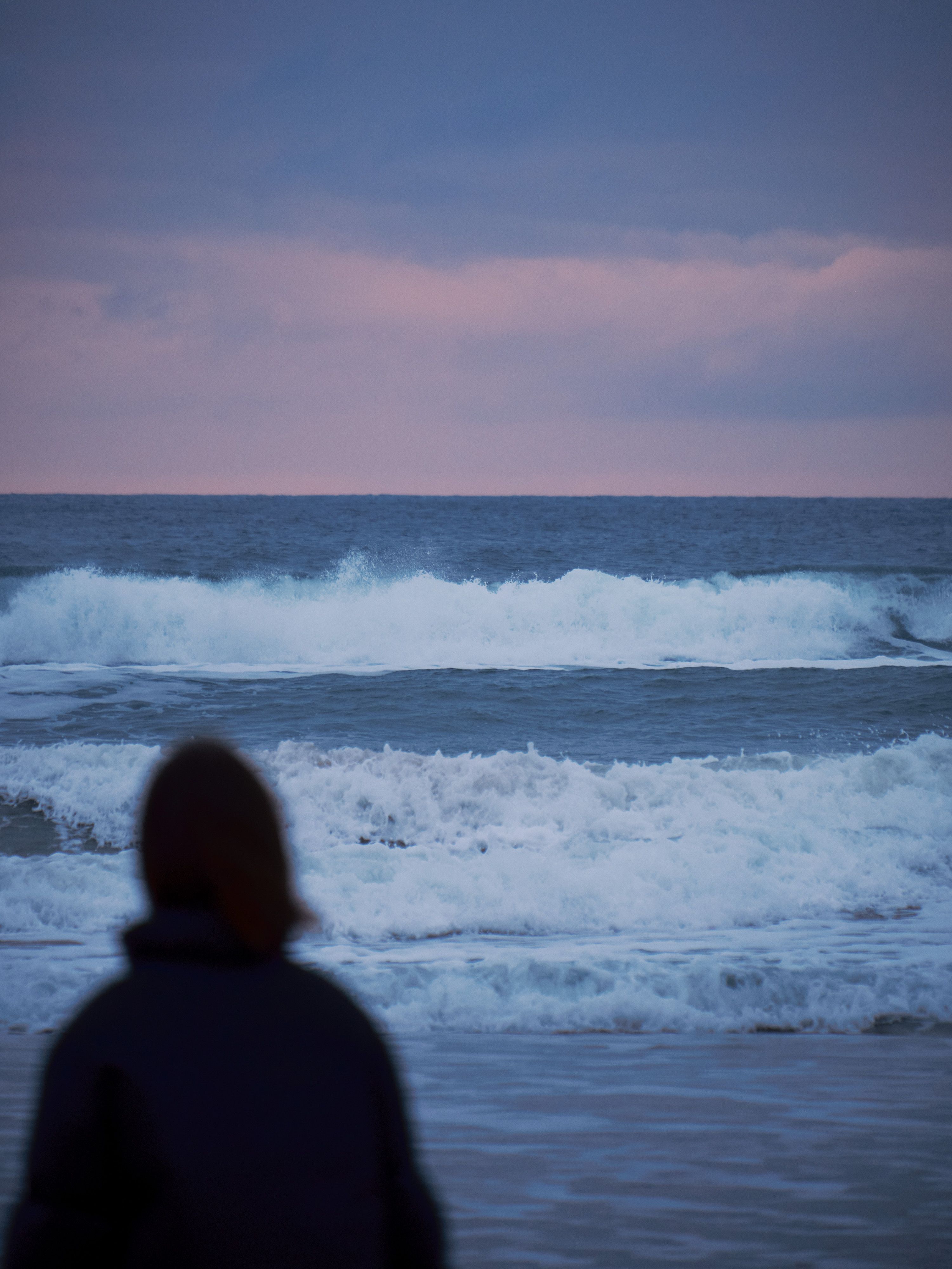 An adult looks out to the rolling waves 