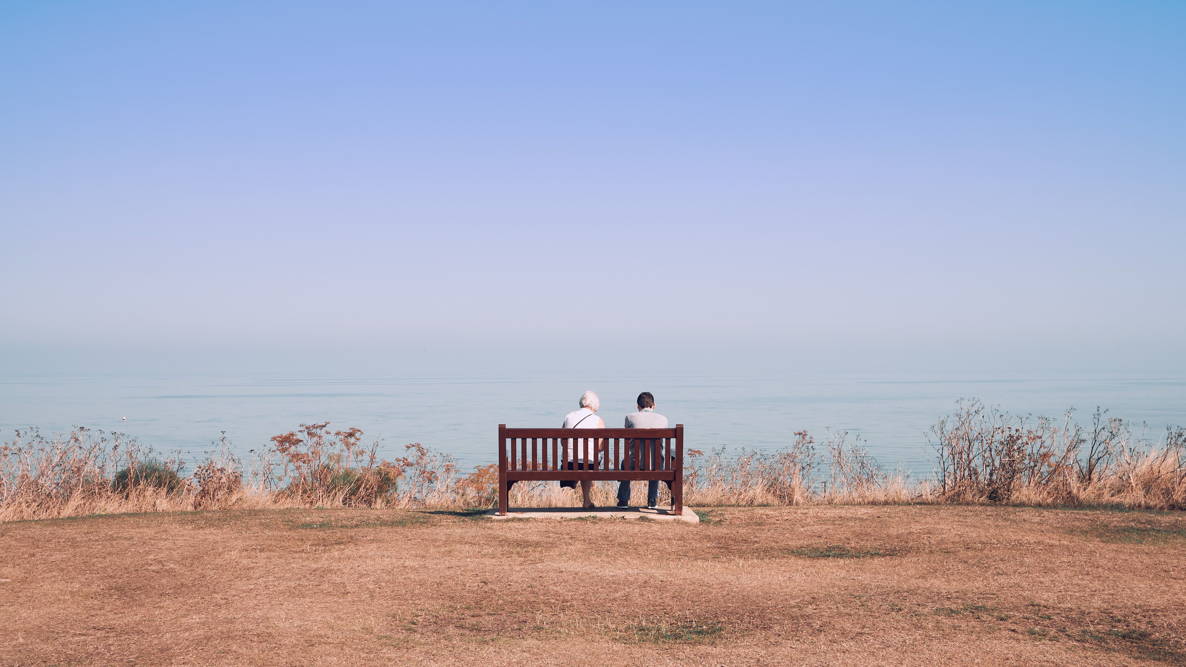 two people sit on a bench looking out to sea