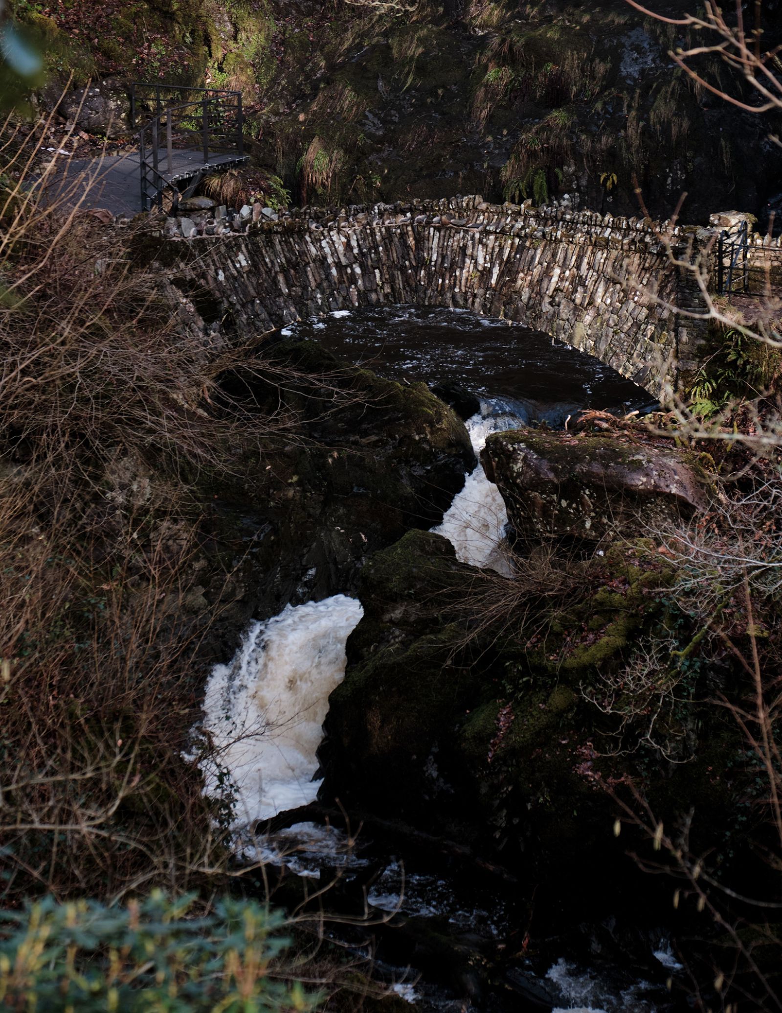 A waterfall snaking under an old stone bridge.