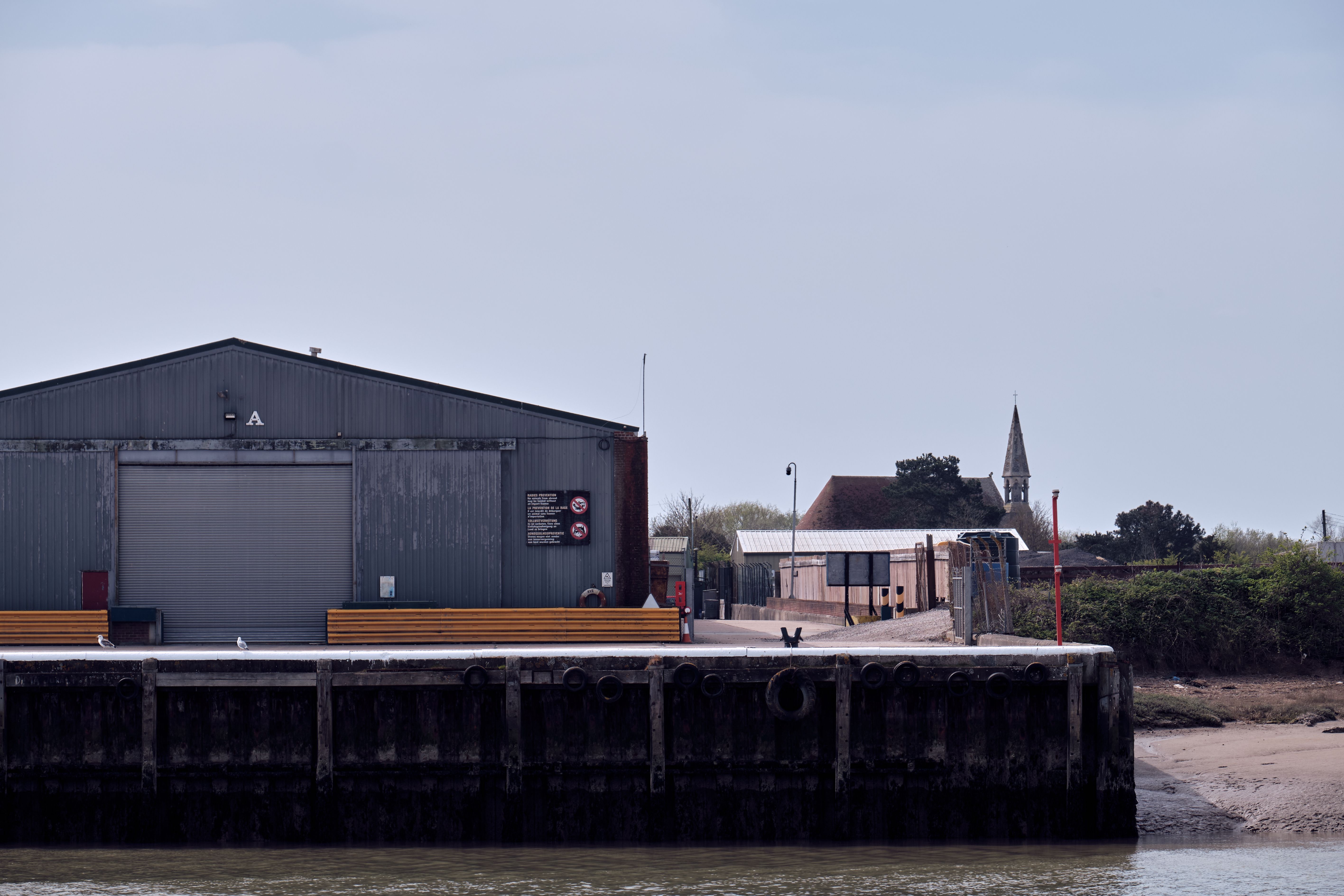 Factory buildings on a dock with a church spire in the background