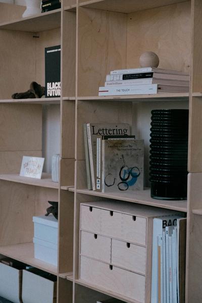 Wooden bookshelves are styled with a variety of branding strategy and design books, black glass vase, wooden objects and drawers, signage and white storage boxes 