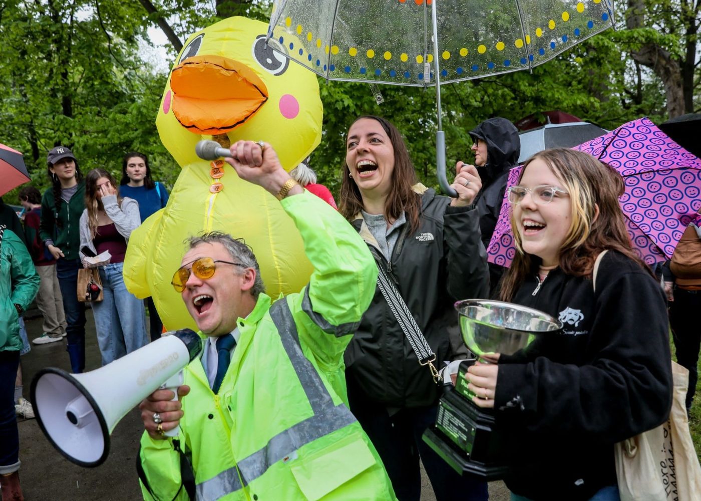 Outdoor duck-race/crowd celebration with bright energy, kids, adults, and a clear public-event feeling.