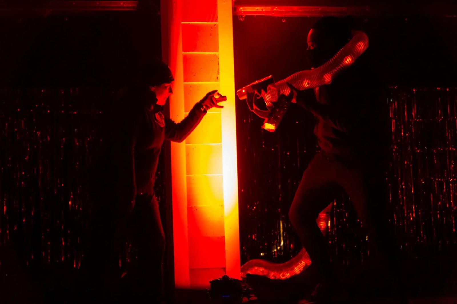 Rachel Alderman and Isaac Bloodworth perform in red light with a translucent serpent puppet in Garage #4 of Boitatá.
