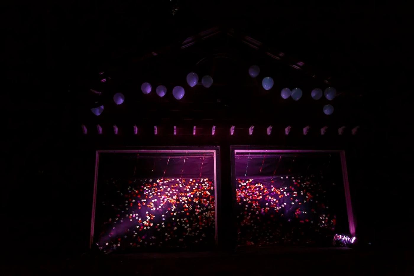 A dark Garage #4 scene from Boitatá with glowing purple light, balloons, and hundreds of small colored eye shapes across the set.