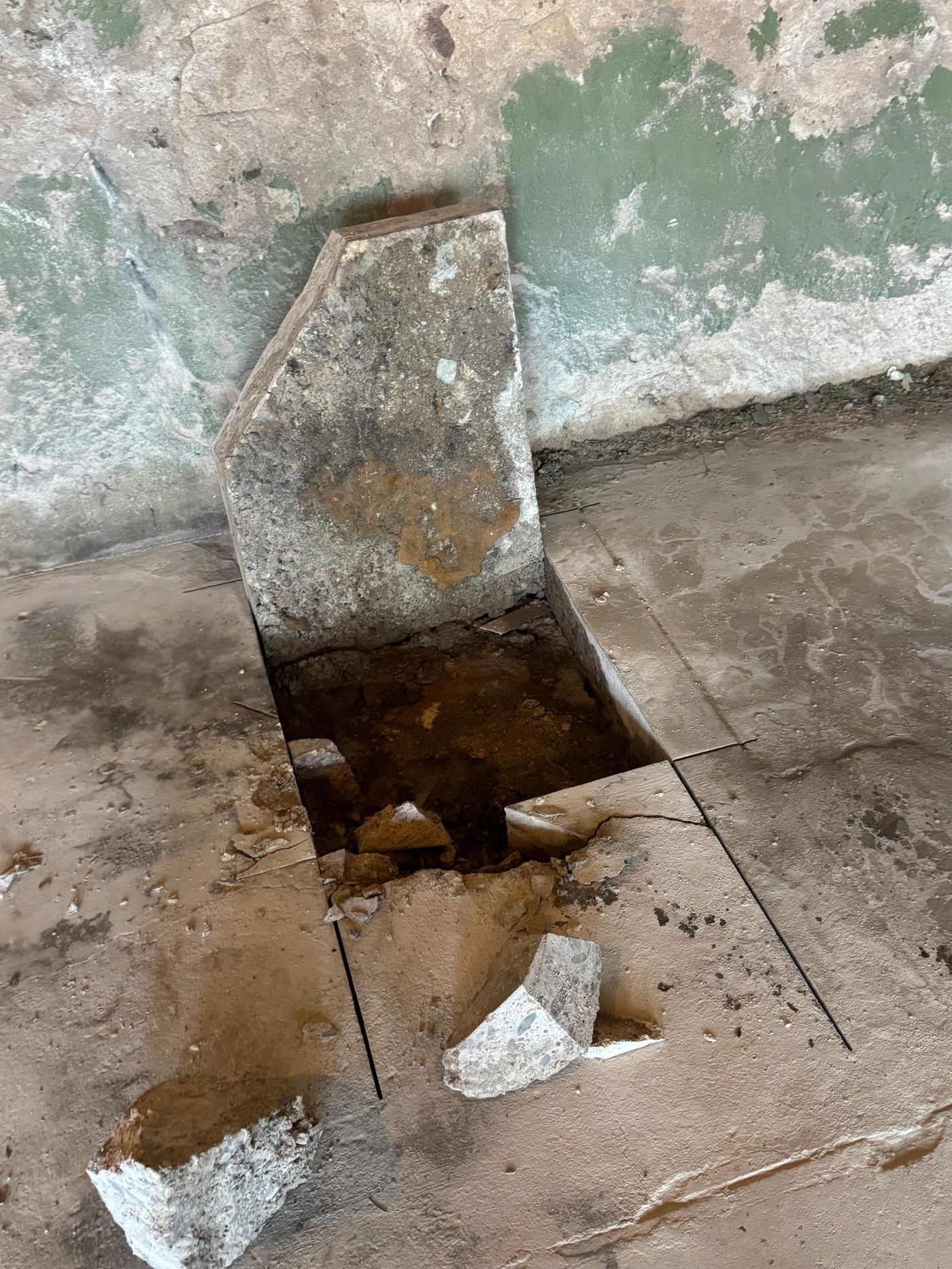 A removed concrete slab leans against a wall beside an opening in the floor, revealing soil beneath at 280 Blake Street.
