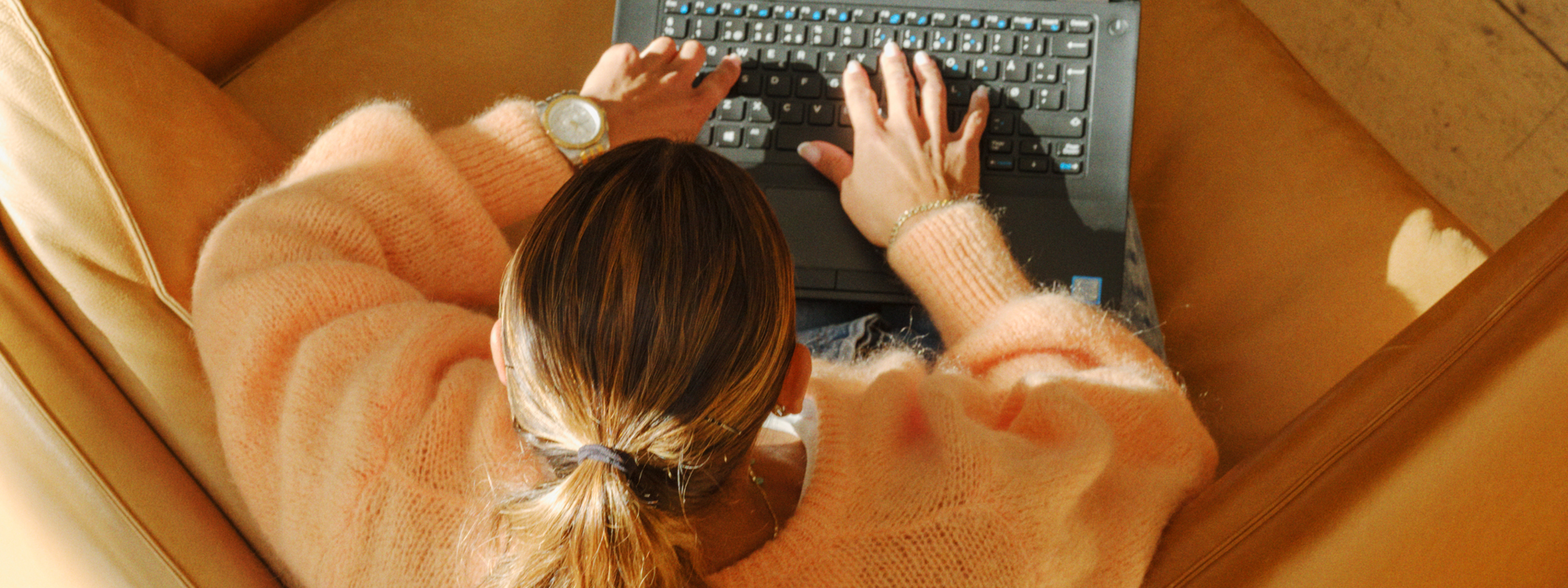 Kvinne som sitter i sofa og jobber på PC