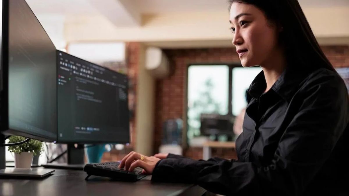 Asian woman typing on a dual monitor setup