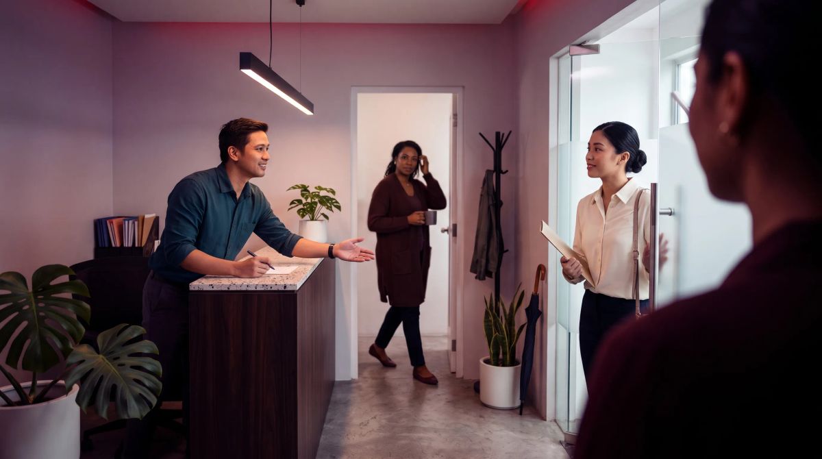 A young applicant pushes open a glass door into a small office as a recruiter rises from his desk to welcome her.