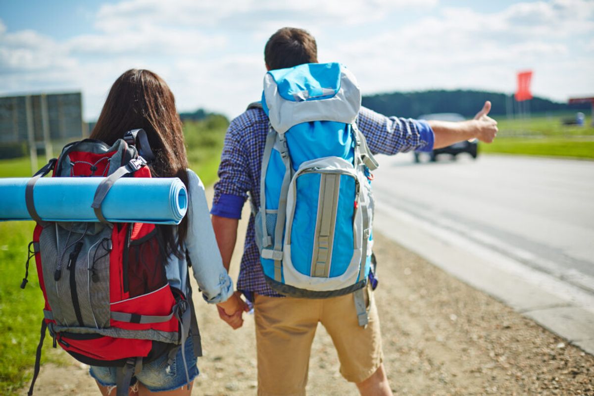 industries affected by recession, young couple of travelers with rucksacks hitch-hiking by road