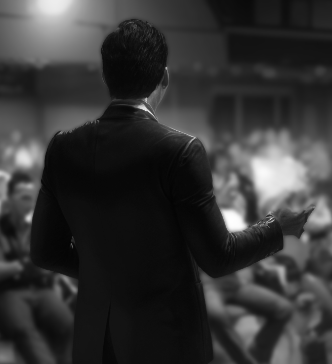 A speaker seen from behind addressing a seated audience.