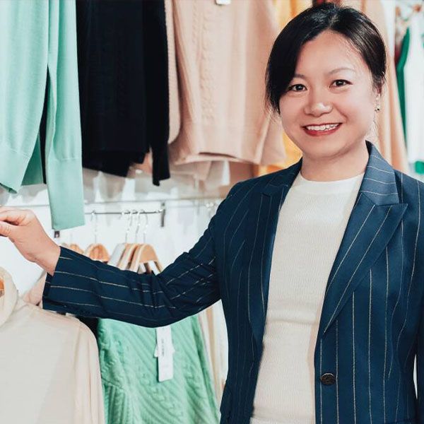 A woman in a striped blazer beside a rack of clothing.