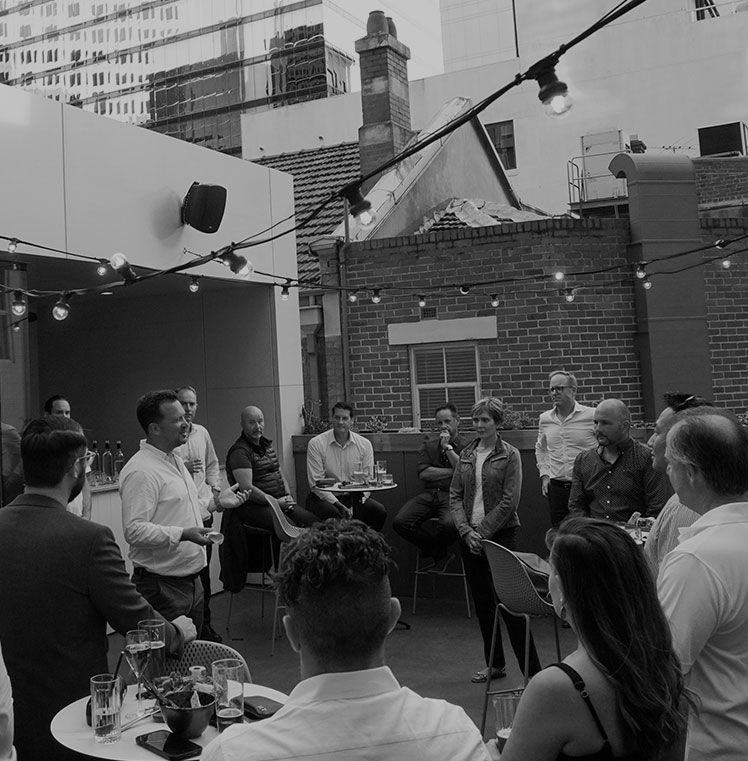 Guests seated at tables in a courtyard strung with festoon lights at an evening launch event.