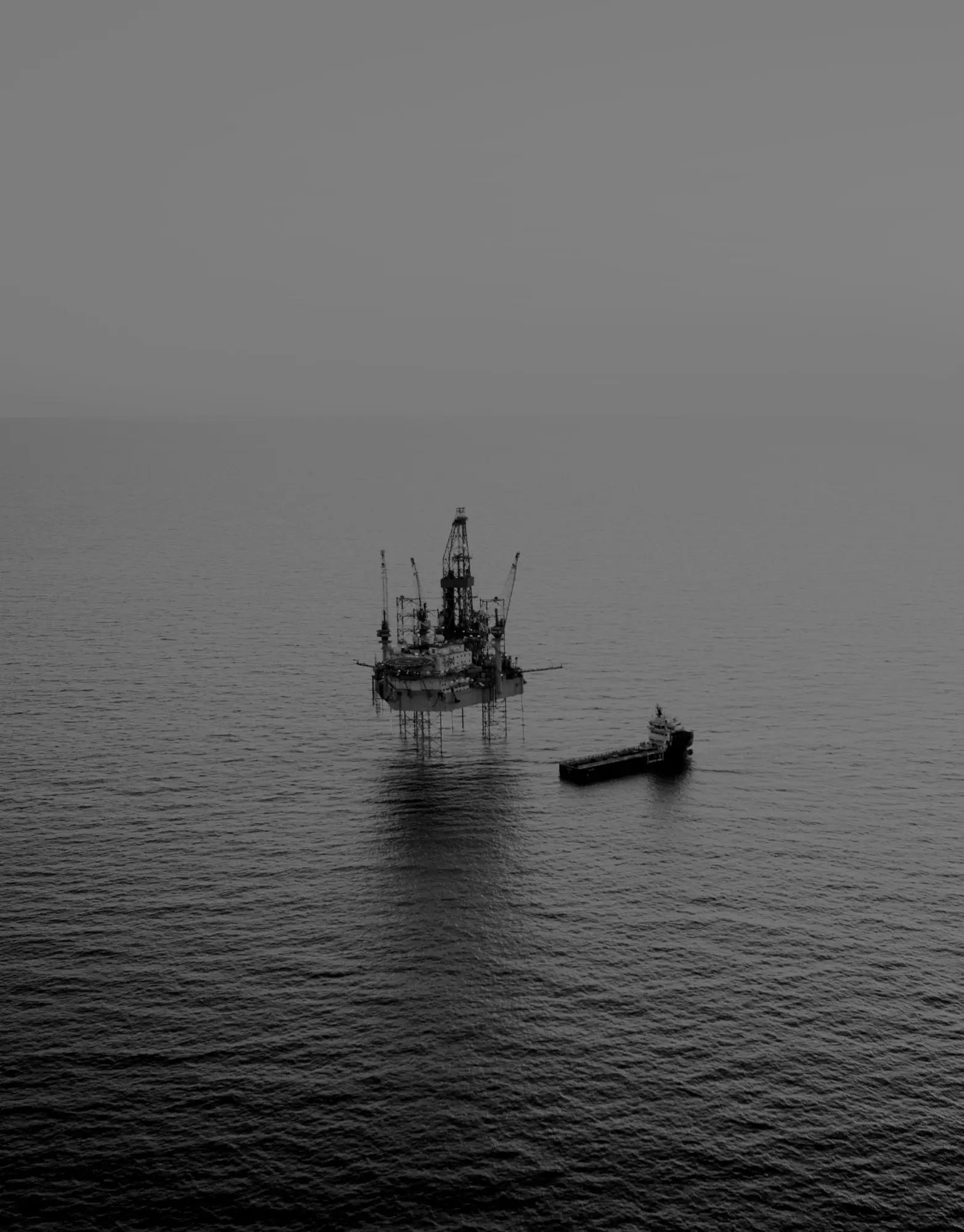 An offshore drilling rig and a support vessel on open water under an overcast sky.
