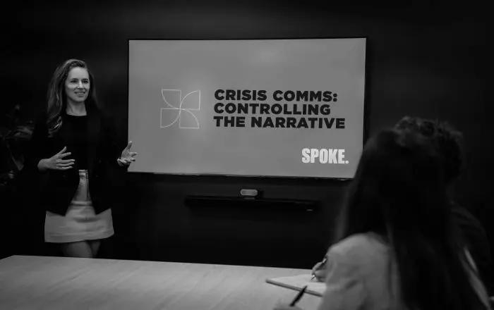 A presenter beside a screen reading "Crisis comms: controlling the narrative", with an attendee taking notes.