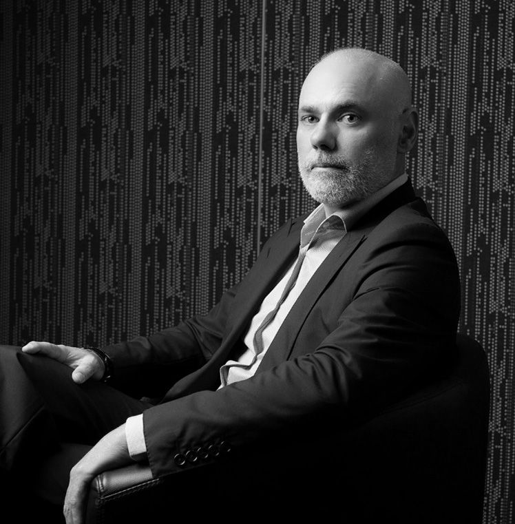 A financial adviser in a dark suit seated against a panelled wall.