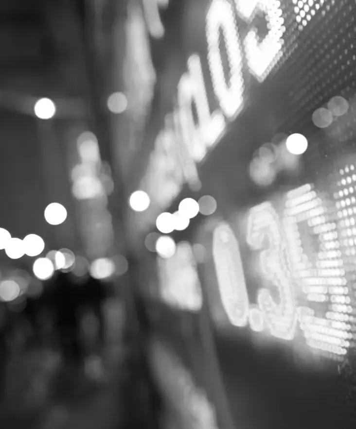 An illuminated share price board at night, with city lights out of focus behind it.