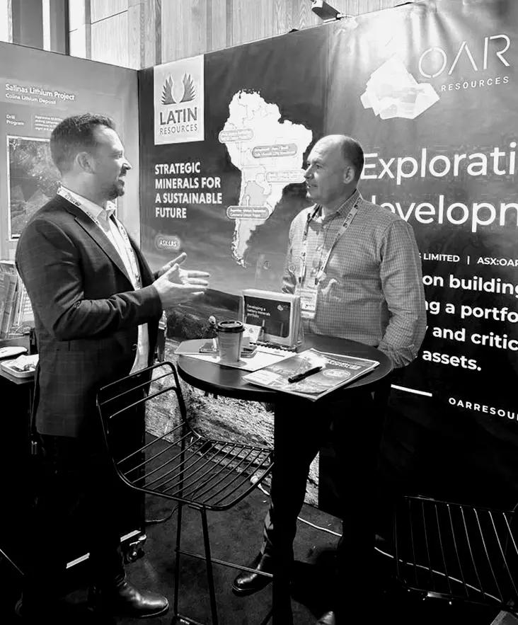 Two delegates talking at a standing table beside an exhibition booth.