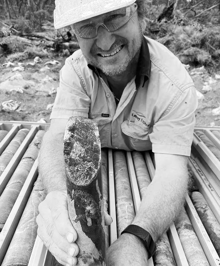 A geologist holding a length of drill core over a core tray.