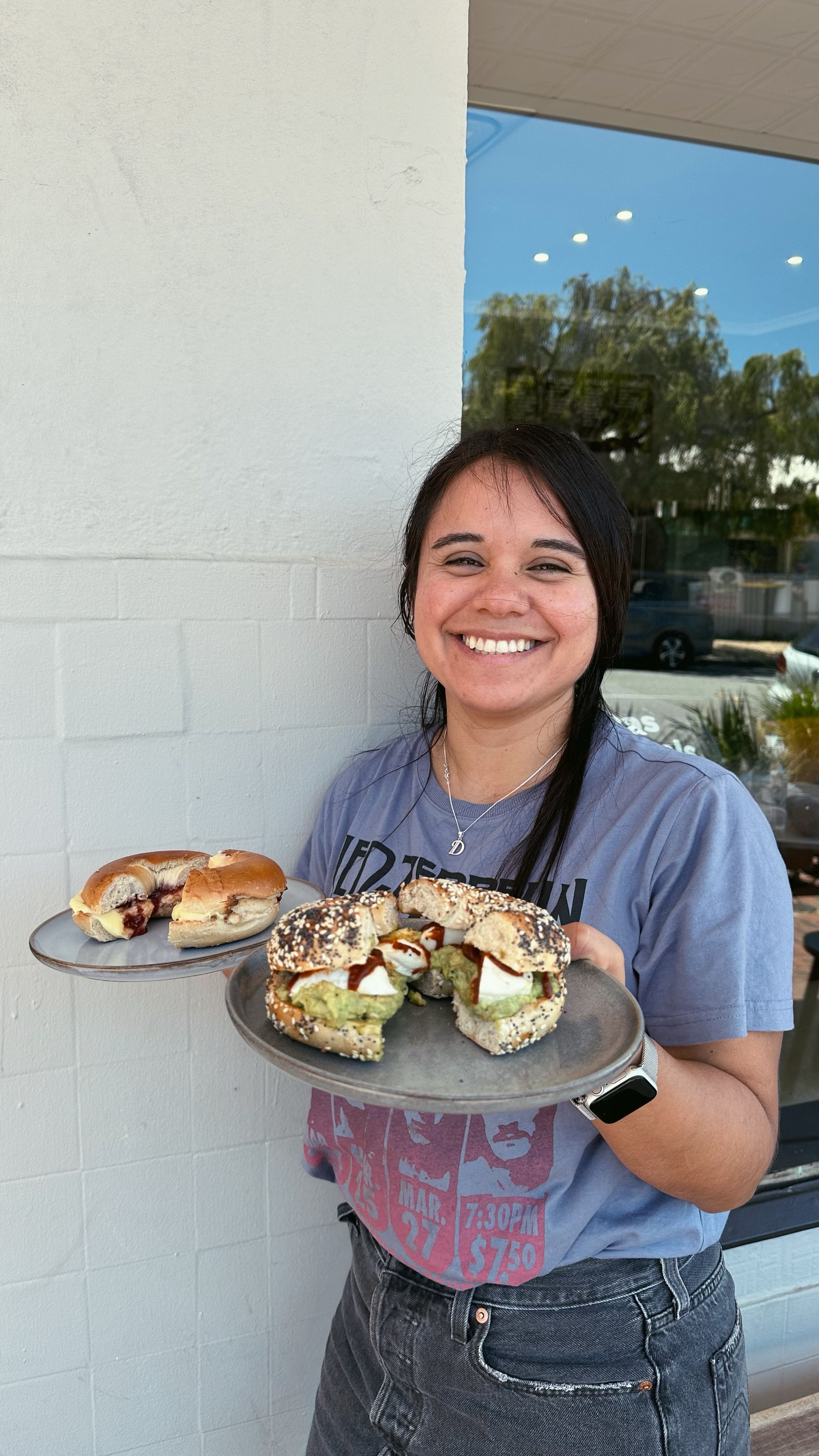 Diana is holding two bagels and smiling at the camera.