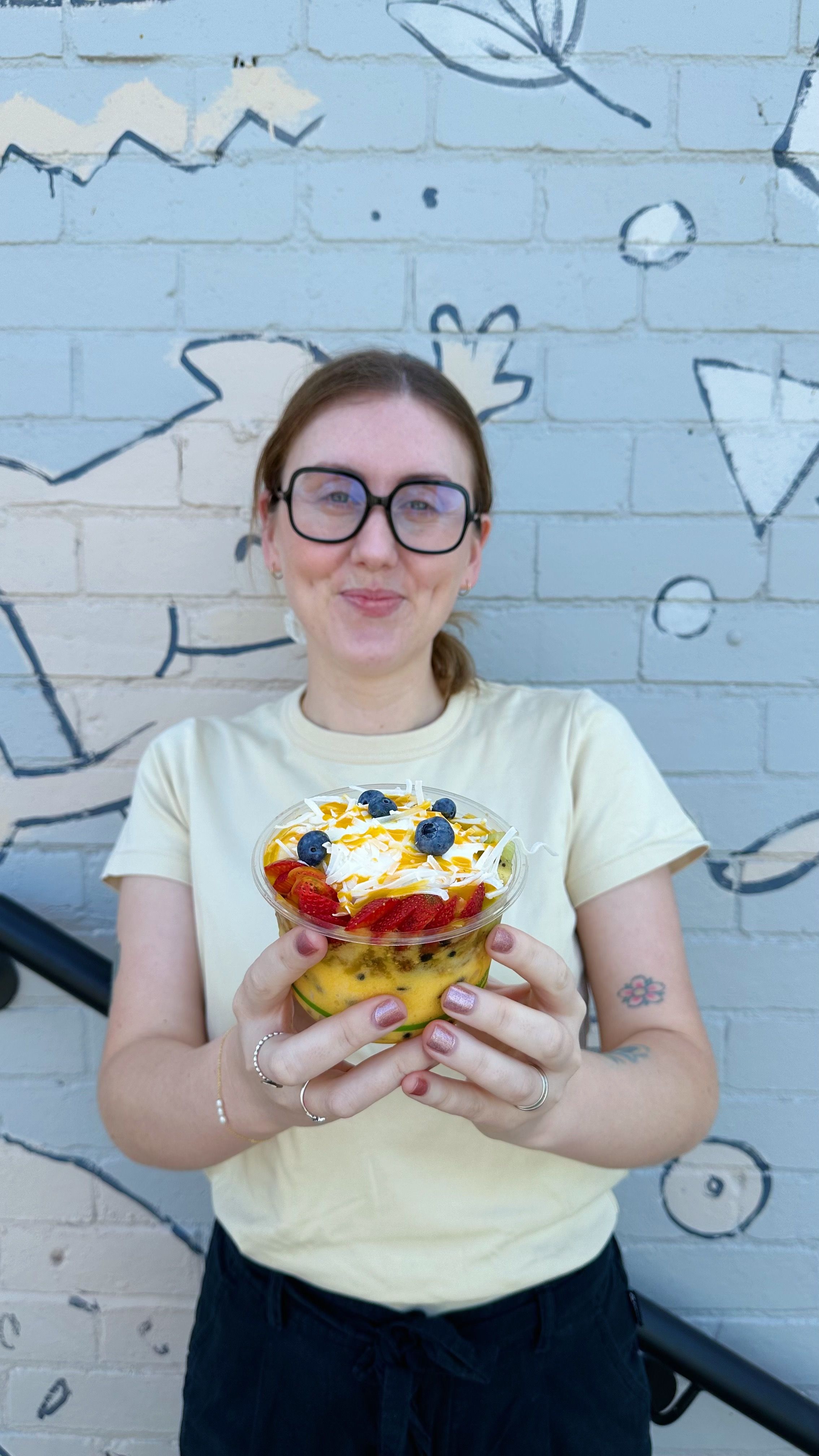 A woman with brown hair is holding a Tropic Like It's Hot bowl with our Tropical Smoothie Base