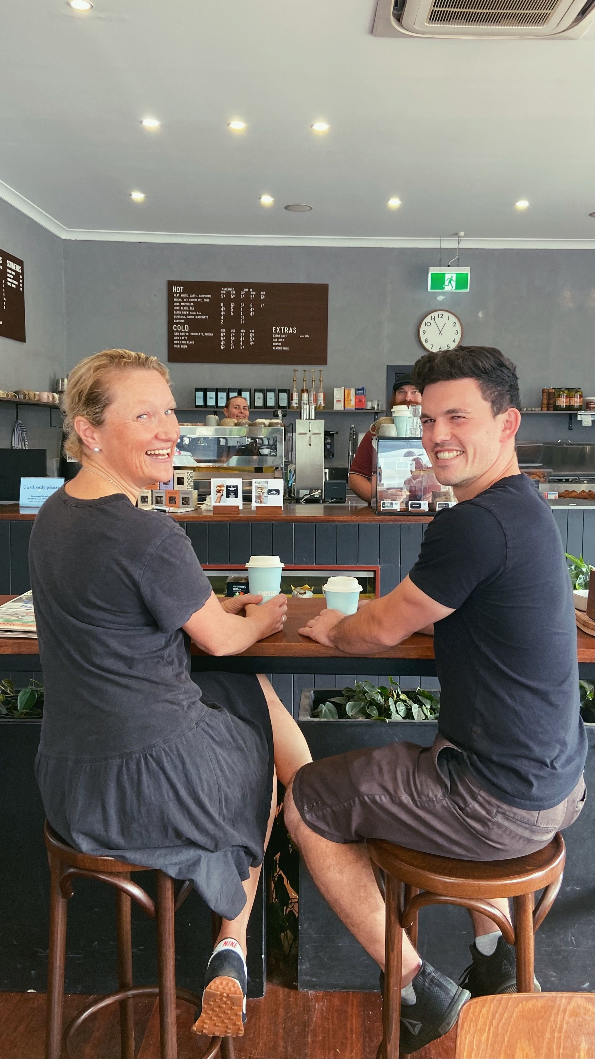 Nash and Keryn are sitting at the front bench with their takeaway coffees. Holly and Yagan are both hiding in the cafe behind them 