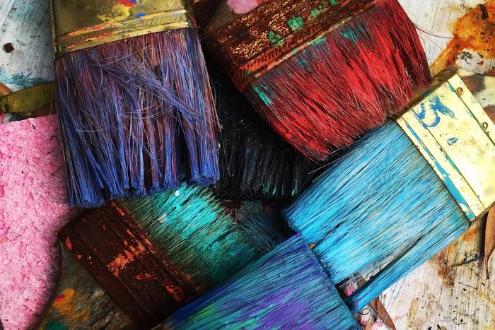 Well-used paintbrushes covered in colorful paint resting on a spattered art table