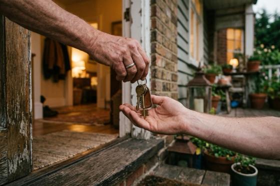 One person handing a set of house keys to another on the doorstep of a warmly lit home