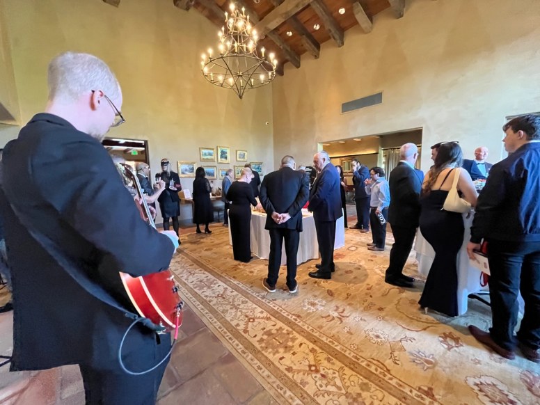 Guests browsing the silent auction beneath a wrought-iron chandelier during the gala's cocktail hour
